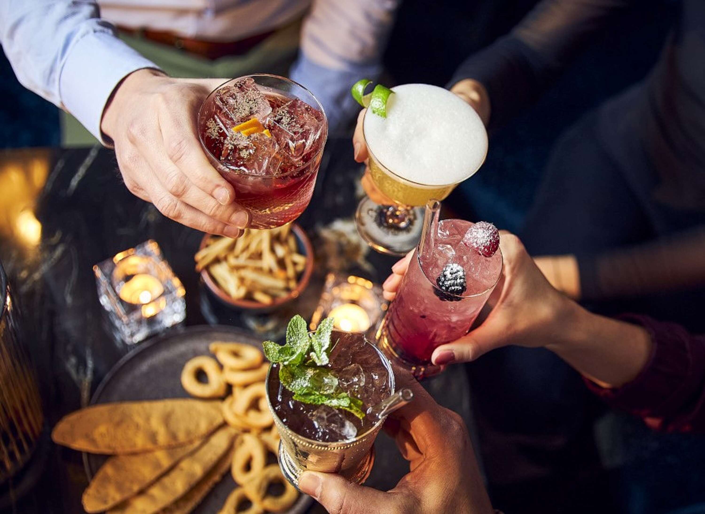 Menschen die mit Cocktail anstoßen über Tisch mit Antipasti und Salzgebäck