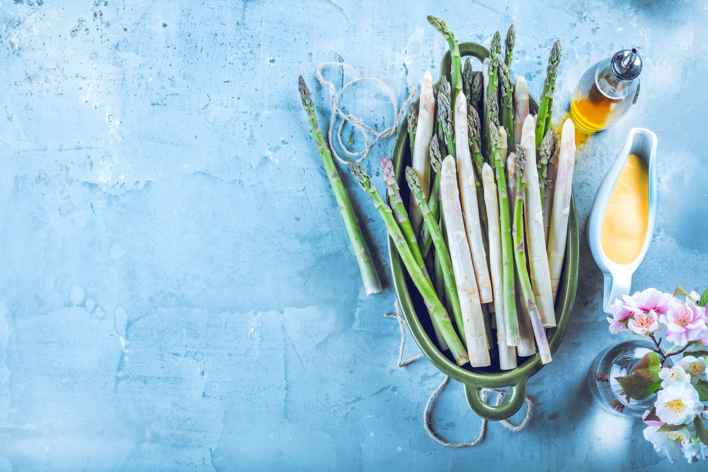 Grüner und weißer Spargel auf einem blauen Tisch mit Sauce Hollandaise